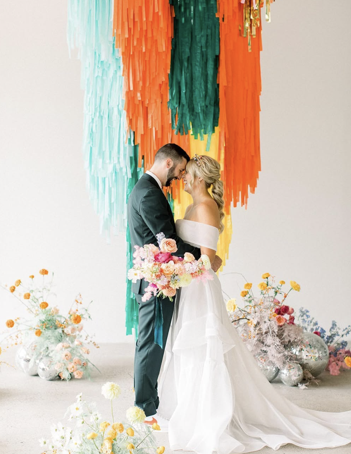 A couple in The White Room in front of a colorful fringe backdrop