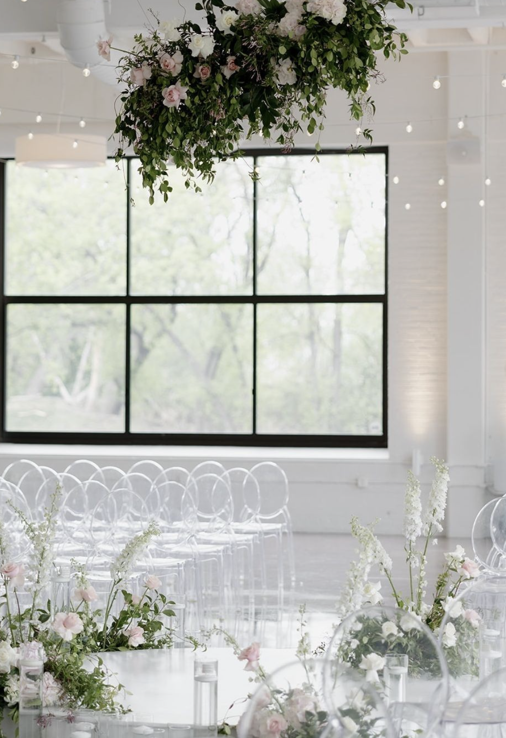 Ceremony in The White Room with ghost chairs, a hanging floral cloud and black framed windows